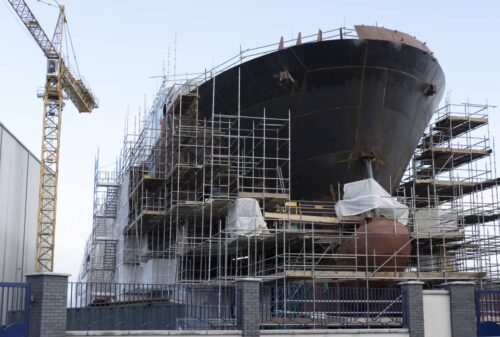 Large Ship Hull Under Construction With Scaffolding and Crane at an Active Shipyard